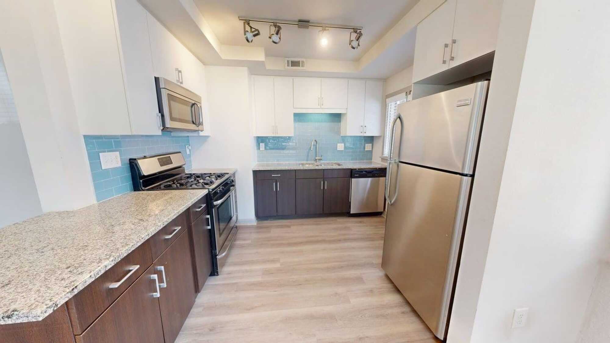 Modern kitchen with white cabinets, stainless steel appliances, granite countertops, and light wood flooring.