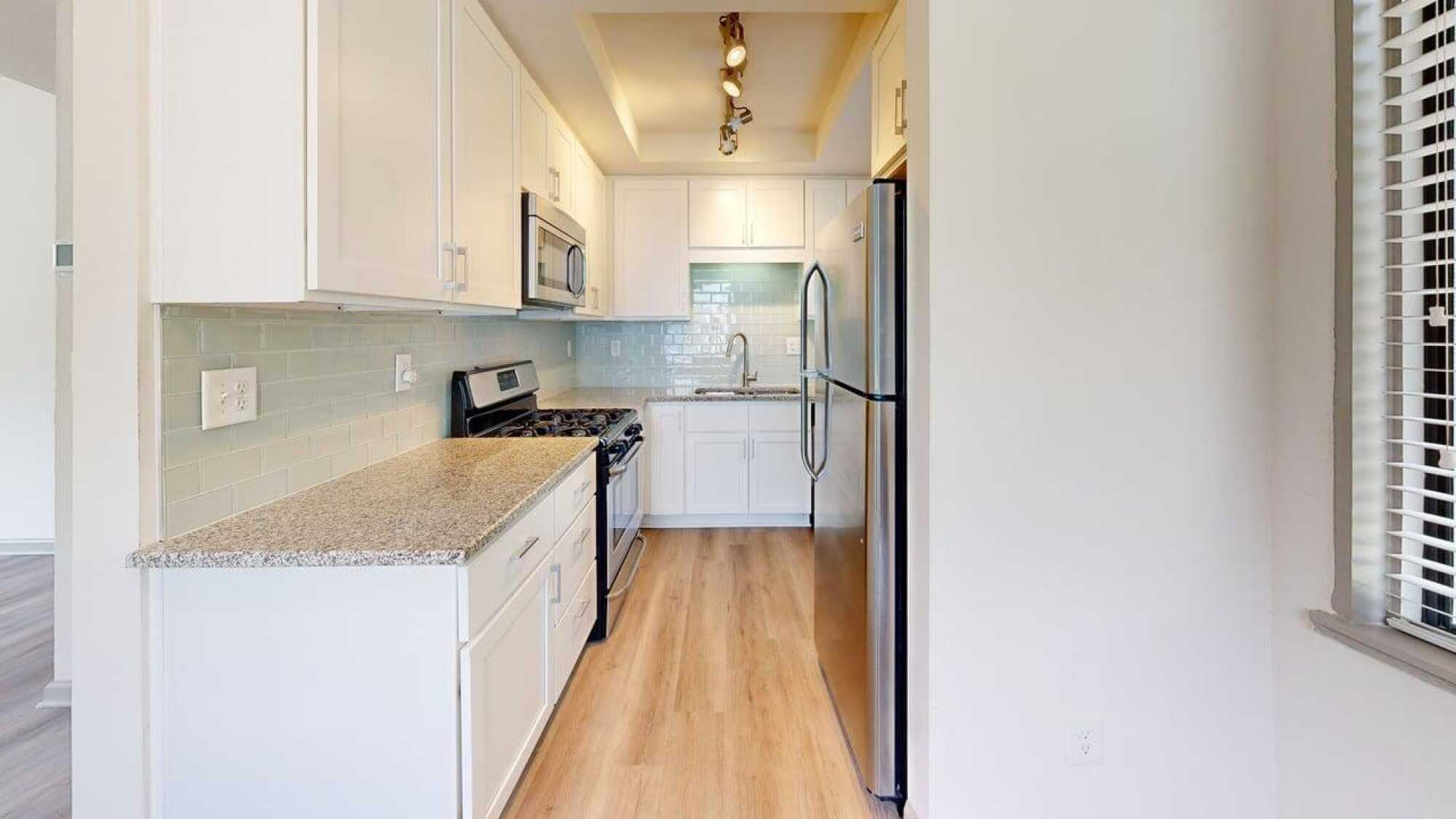 Modern kitchen with white cabinets, stainless steel appliances, granite countertops, and light wood flooring.